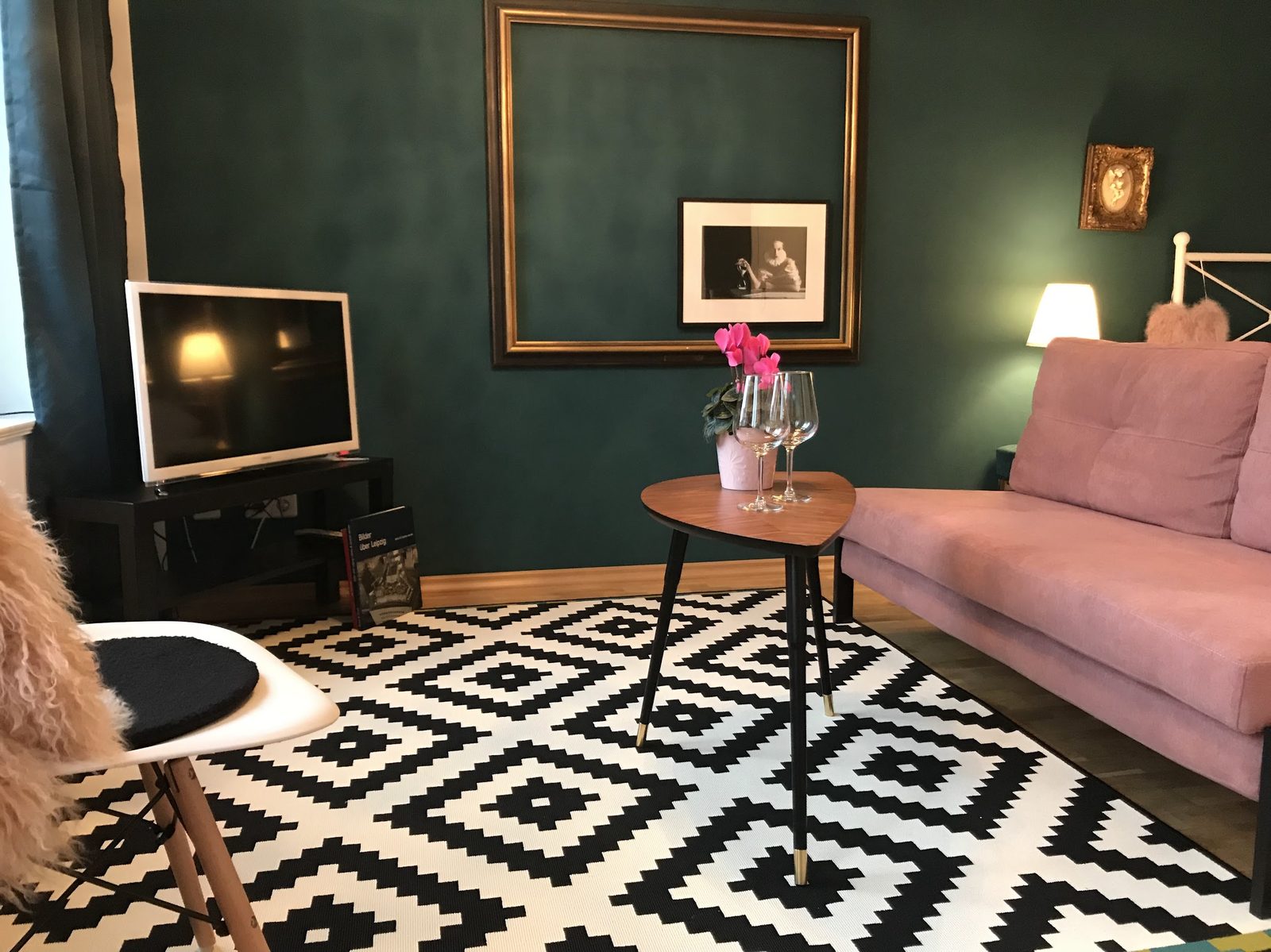 Wohnzimmer von Wohnung 1 mit petrolfarbenen Wänden, goldgerahmtem Bild und rosa Samtsofa